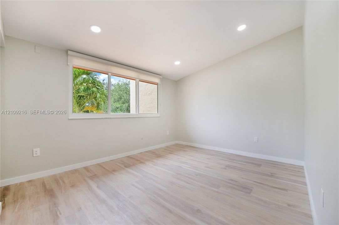Neutral interior space featuring recessed ceiling lighting, light-toned wood-finish flooring, and a window with exterior vegetation
