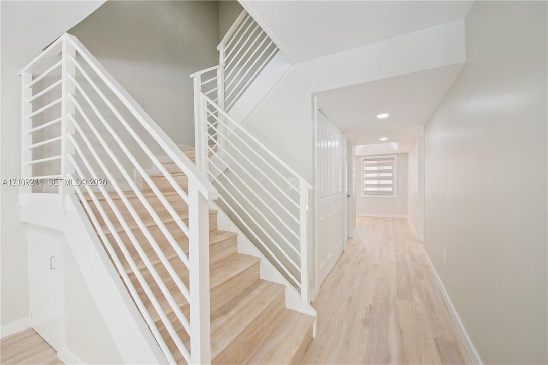 Staircase featuring white horizontal-bar railings, wood-finish treads, neutral wall paint, recessed lighting, and wood-finish flooring