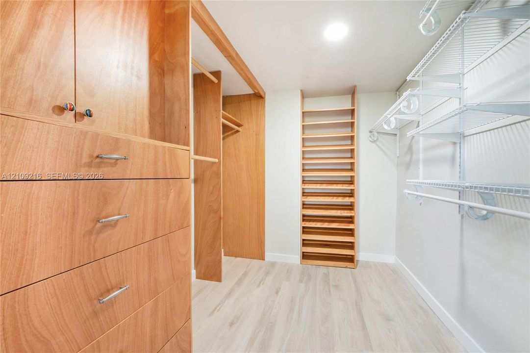 Walk-in closet featuring custom wood cabinetry with integrated dresser drawers, full-height open shelving, wood-finish flooring, and white wire shelving systems