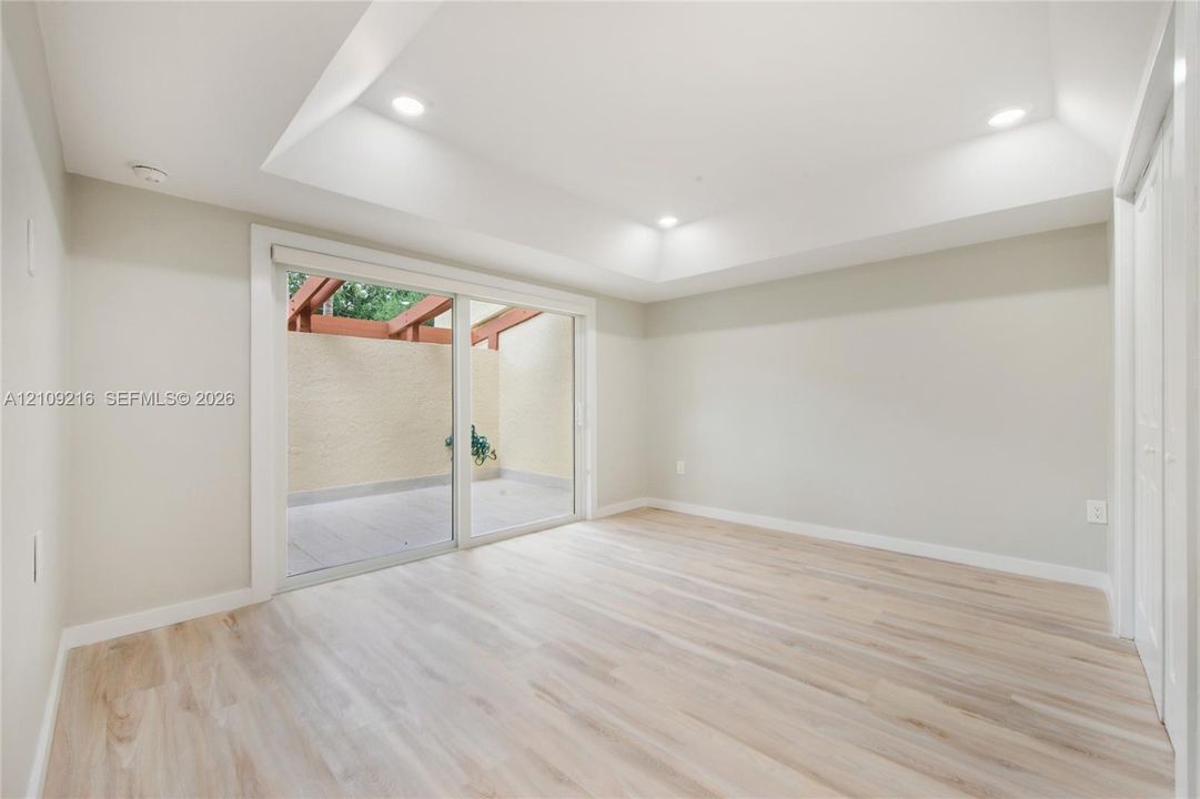 Tray ceiling with recessed lighting, wood-finish flooring, and sliding glass doors opening to a private patio featuring a wood pergola