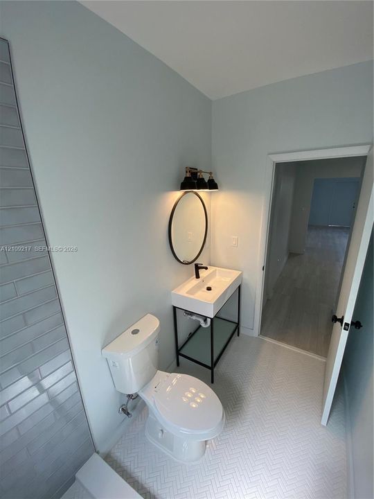 Wall-mounted vanity with a rectangular sink, black metal console frame, matching circular mirror, and white herringbone floor tile