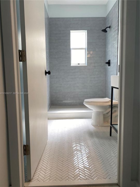 Bathroom featuring herringbone-patterned tile flooring, subway-tiled shower surround, and matte black plumbing fixtures