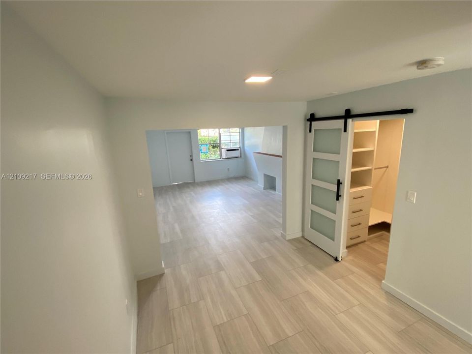 Light-toned tile flooring throughout, sliding barn door with frosted glass panels, and built-in closet cabinetry featuring shelving and drawers