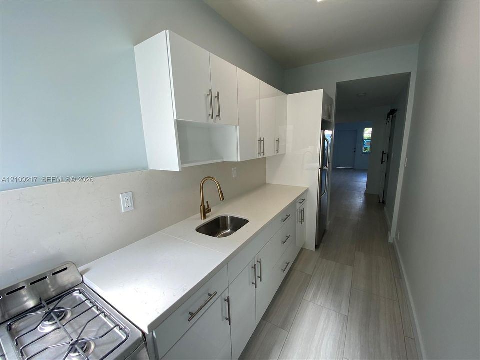 Kitchen featuring white cabinetry, solid-surface countertops, metallic-finish faucet, stainless steel under-mount sink, and wood-finish flooring