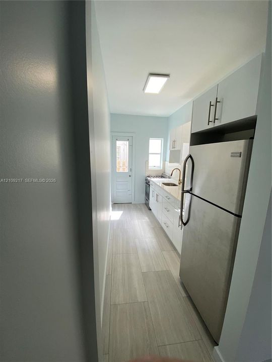 Kitchen featuring white cabinetry, stainless steel refrigerator, stone-finish countertops, wood-finish tile flooring, and flush-mount ceiling lighting