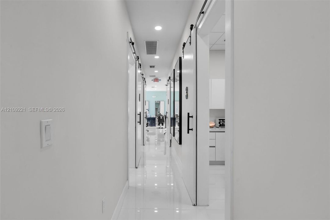 Hallway featuring polished white tile flooring, recessed lighting, and multiple white barn-style sliding doors with matte black hardware