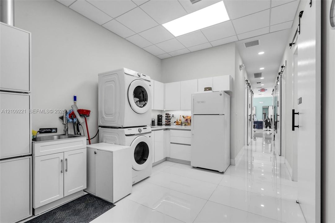 Utility space featuring white shaker-style cabinetry, a stainless steel undermount sink, glossy tile flooring, and integrated white appliances