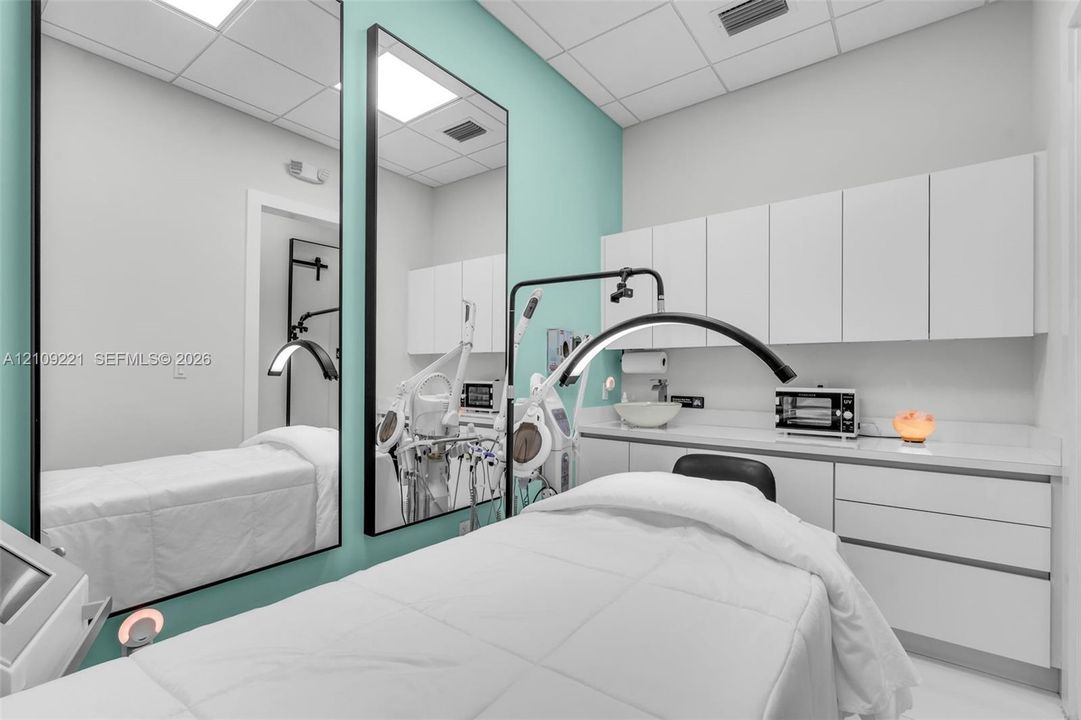 Room featuring high-gloss built-in cabinetry, expansive wall-mounted mirrors, drop-ceiling grid, and integrated countertop with vessel sink