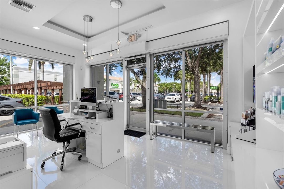 Floor-to-ceiling glass storefront windows, polished tile flooring, recessed ceiling lighting, custom built-in shelving with integrated lighting, and modern multi-pendant light fixtures