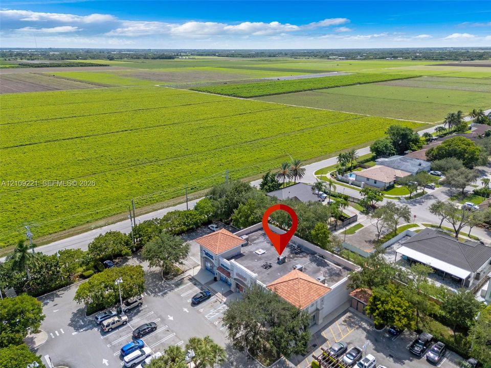 Commercial property featuring a red tile roof, dedicated parking area, and direct exposure to expansive agricultural acreage