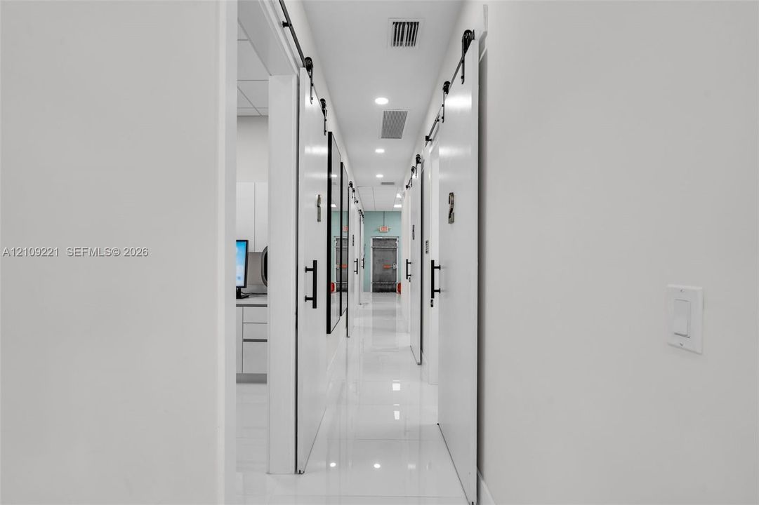 Hallway featuring polished tile flooring, white sliding barn-style doors with matte black hardware, and recessed ceiling lighting