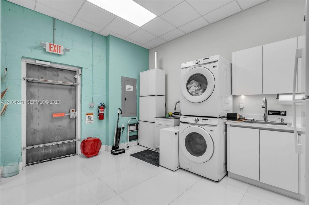 Utility area featuring high-gloss tile flooring, stacked laundry appliances, white cabinetry with integrated sink, and recessed ceiling panels
