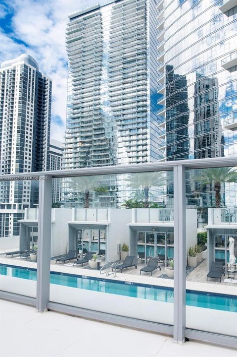 Swimming pool with a glass panel railing, paved sun deck, and structural cabana-style enclosures