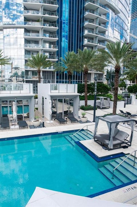 Swimming pool with integrated tanning ledge and stairs, surrounding hardscaped sun deck, private poolside cabanas, and mature palm landscaping
