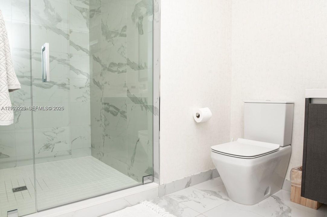 Walk-in shower with floor-to-ceiling stone-finish tile surround, frameless glass enclosure, and white tile flooring