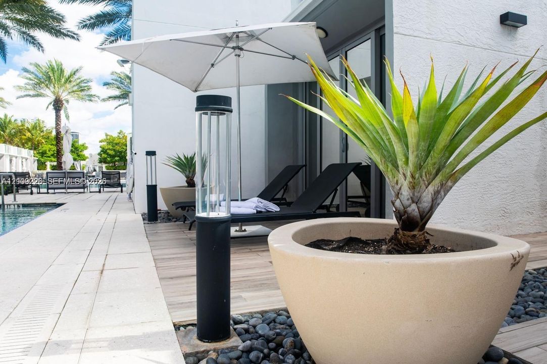Outdoor patio featuring wood-finish decking, smooth stucco exterior walls, hardscaped stone pathways, and integrated cylinder landscape lighting