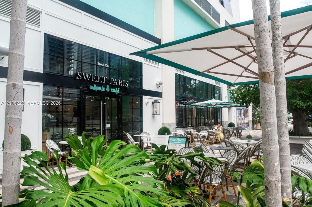 Commercial storefront featuring floor-to-ceiling glass windows, black metal framing, integrated wall-mounted lighting, and a paved outdoor patio area