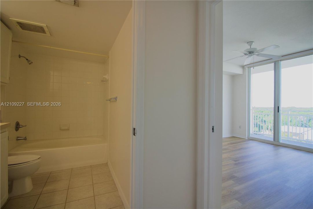 Bathroom featuring a white tile tub surround and ceramic floor tiling, wood-finish flooring, floor-to-ceiling glass sliding doors, and a ceiling fan
