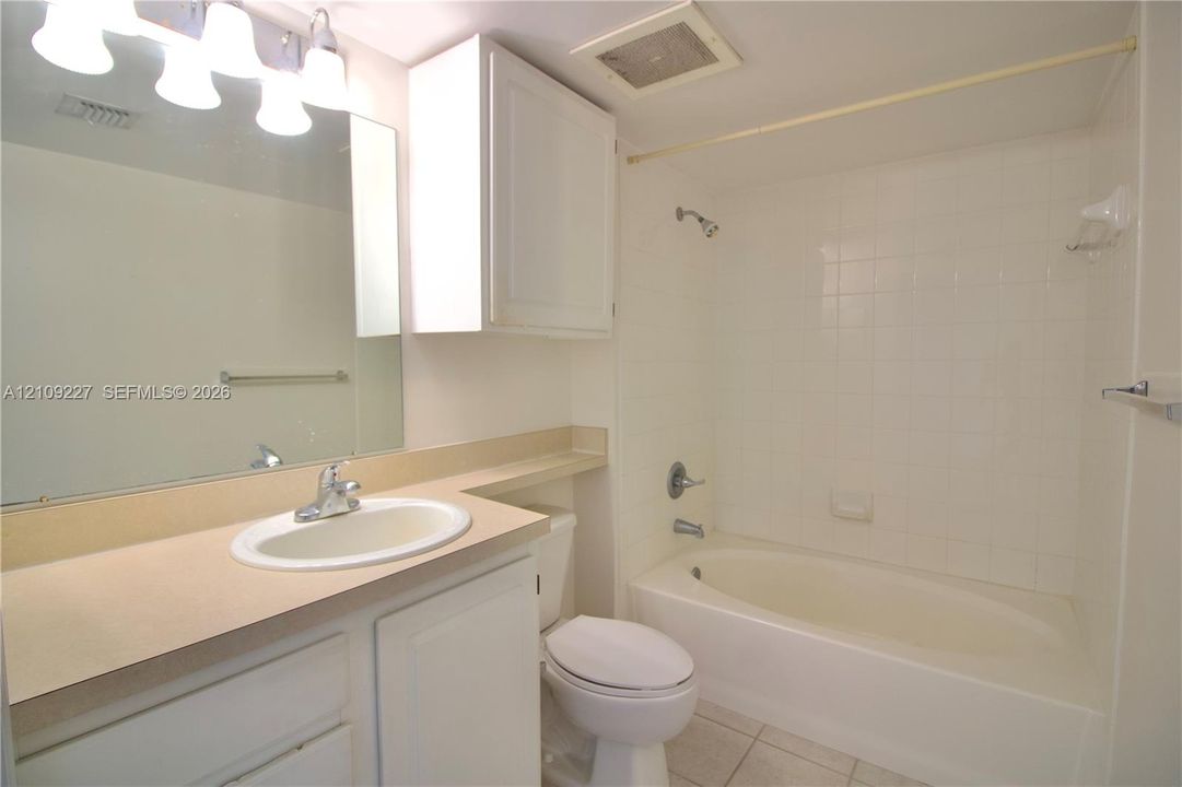 Bathroom featuring a vanity with a solid-surface countertop, an oval inset sink, a large wall-mounted mirror, a tiled shower-tub combination, and white built-in cabinetry