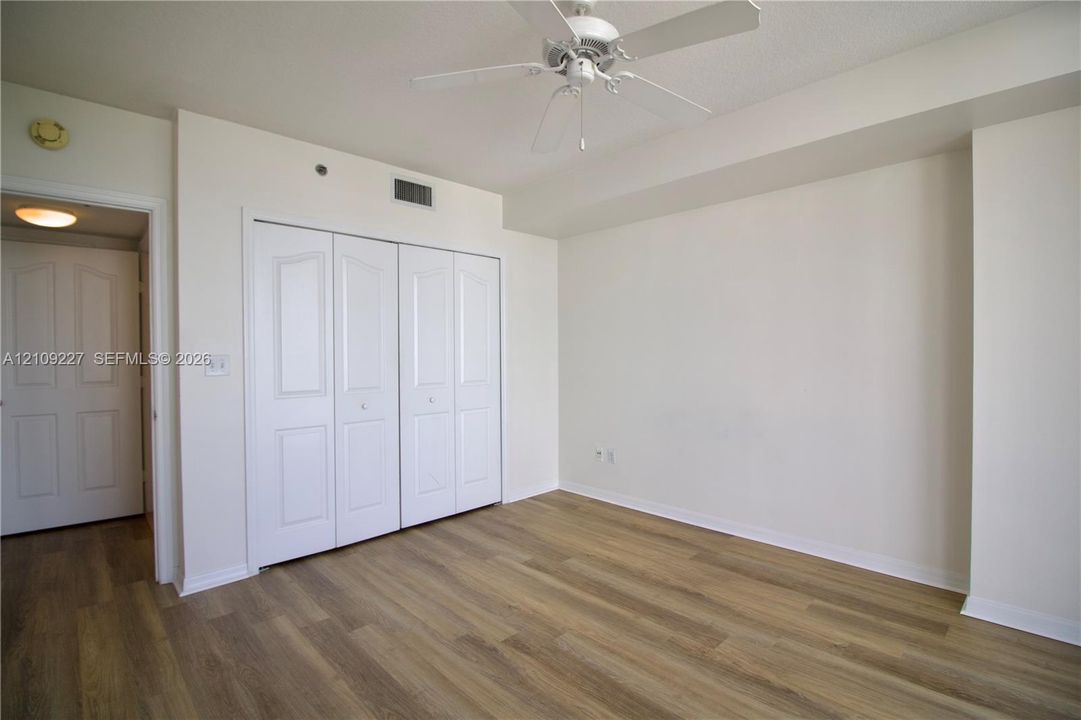 Interior room featuring wood-finish flooring, white four-panel closet doors, and a ceiling-mounted fan with integrated light fixture
