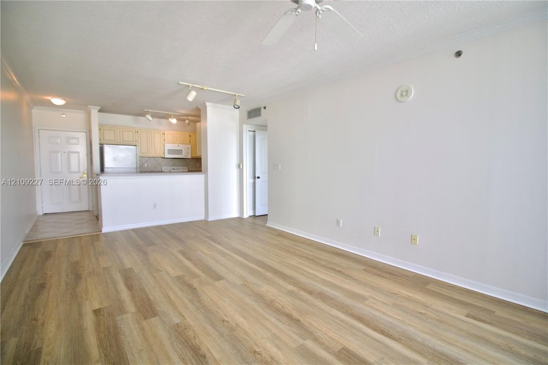 Open-concept floor plan featuring wood-finish flooring, recessed track lighting, ceiling fan, and built-in cabinetry with stainless steel appliances