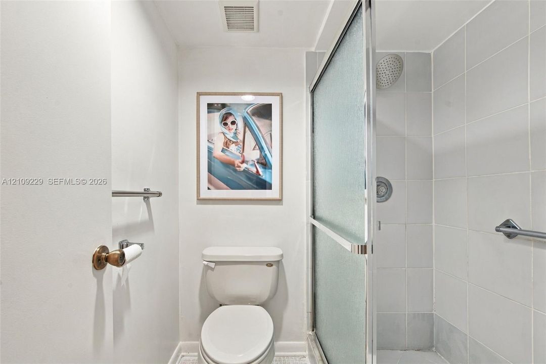 Full bathroom featuring a glass-enclosed shower with tiled surround, wall-mounted hardware, and a standard toilet