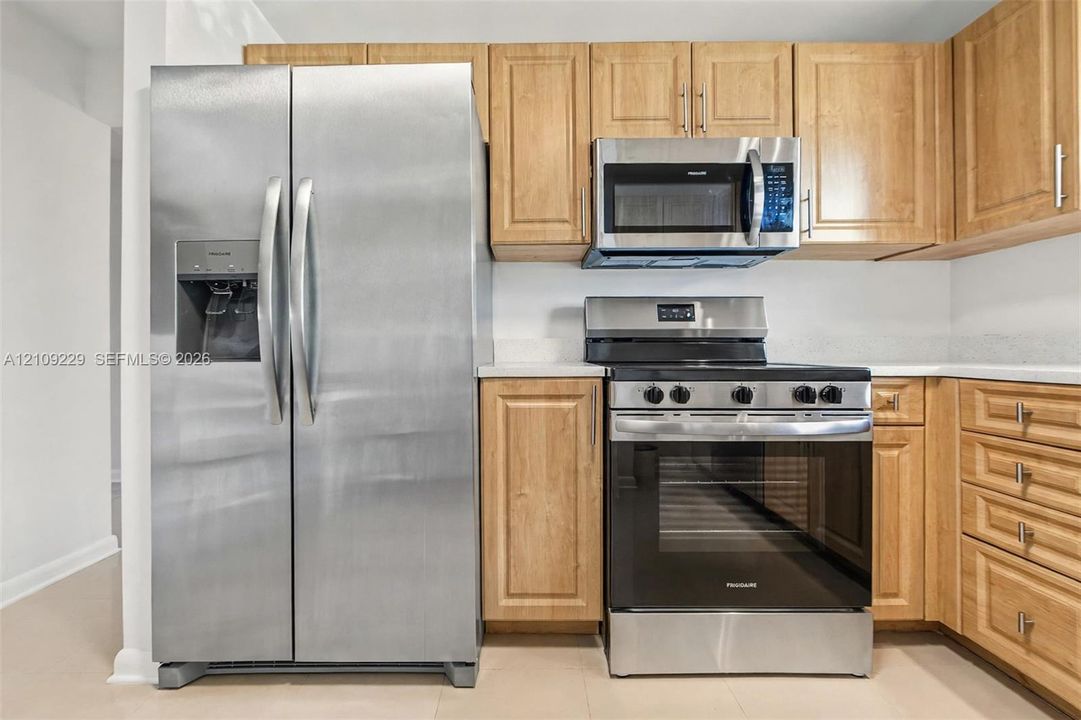 Kitchen featuring wood cabinetry, stainless steel side-by-side refrigerator, stainless steel microwave, and stainless steel slide-in range