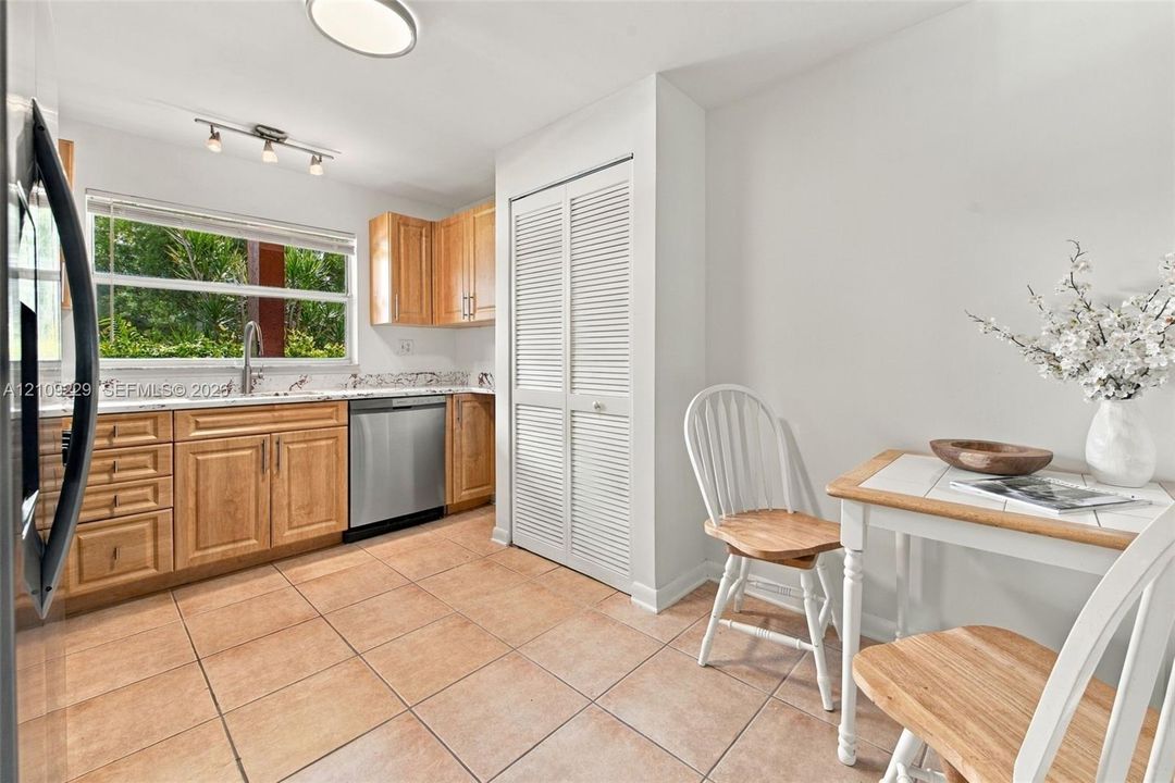 Kitchen featuring natural wood cabinetry, stainless steel dishwasher, tile flooring, and louvered double-door pantry
