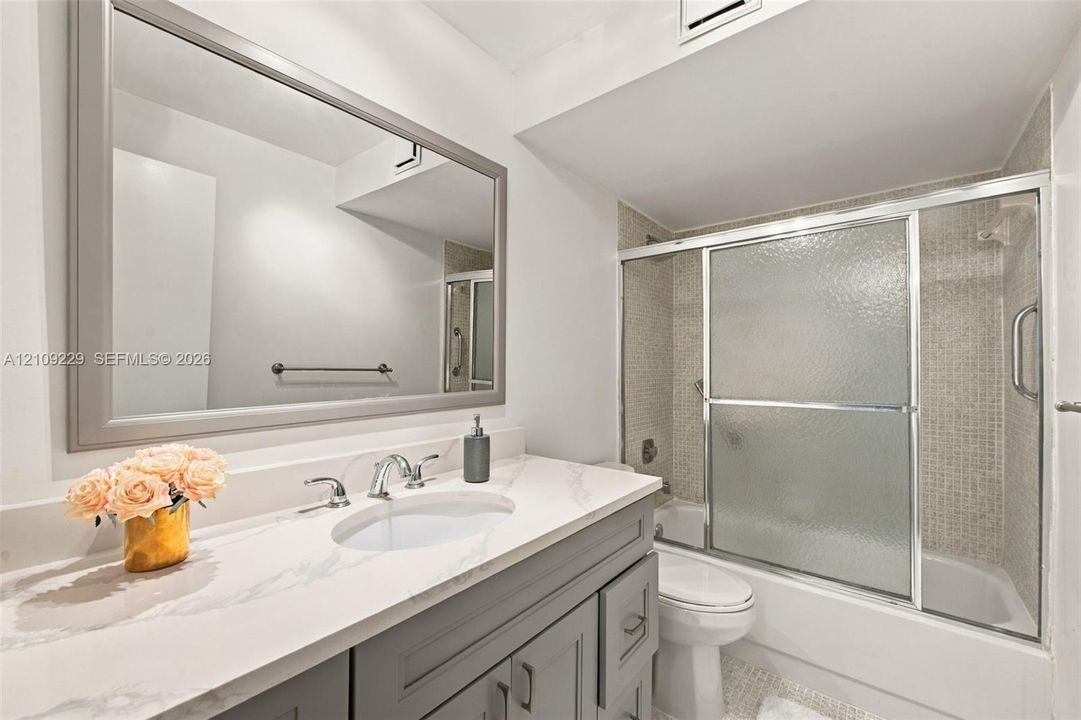 Bathroom featuring a vanity with a light-toned stone countertop, undermount sink, and brushed metal faucet, paired with a large framed mirror and a bathtub-shower combination with sliding glass doors