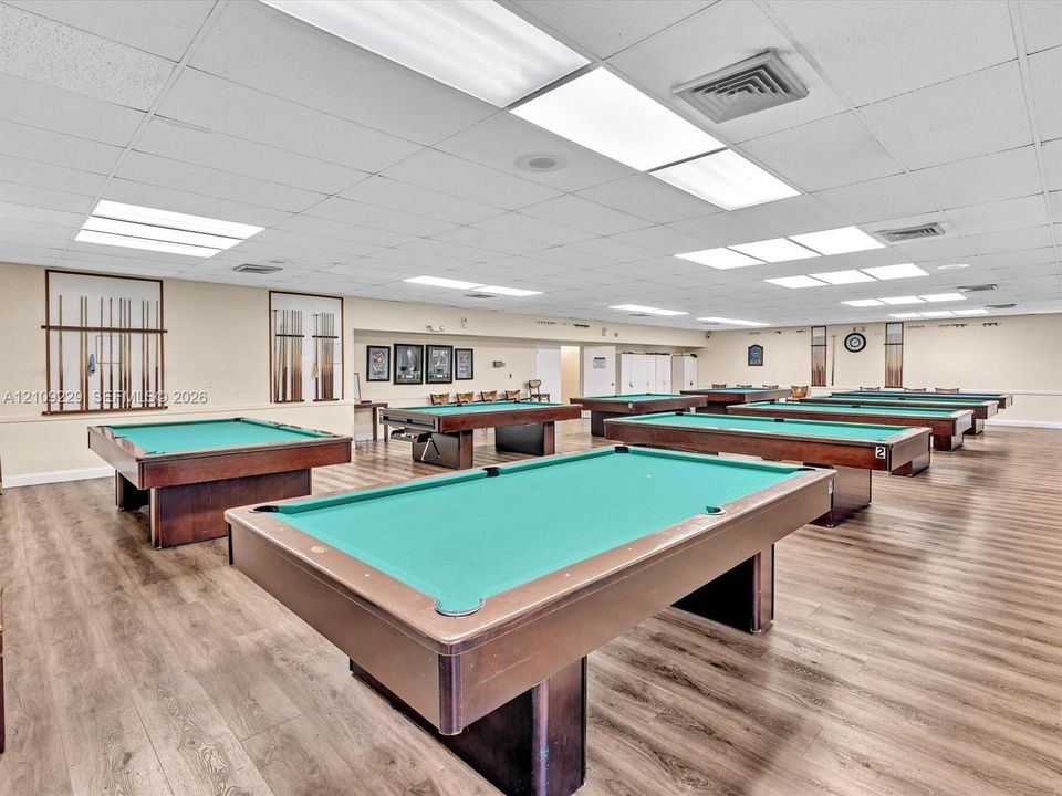 Large room featuring wood-finish flooring, drop ceiling with integrated rectangular lighting, and built-in wall-mounted cue racks