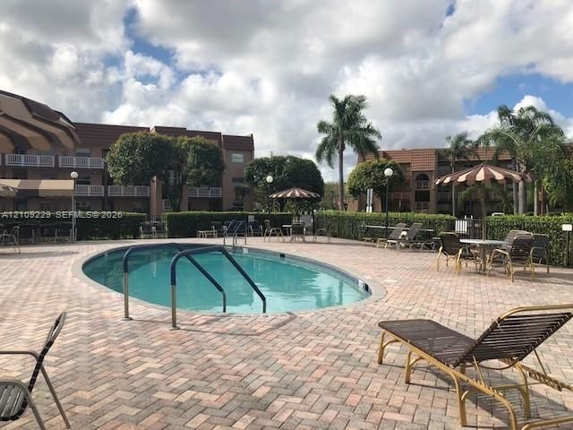 Oval swimming pool featuring a brick-paver deck, metal safety railings, and perimeter hedging
