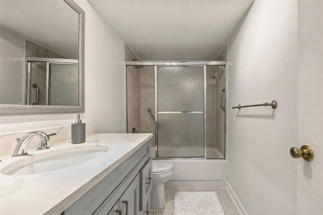 Bathroom featuring a gray vanity cabinet, white countertop with an integrated basin, chrome faucet, tiled shower surround, and sliding glass shower doors