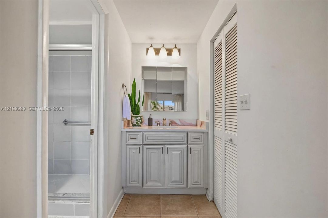 Bathroom featuring a vanity with raised-panel cabinetry, tile countertop, triple-light fixture, medicine cabinet, and bifold louvered closet doors