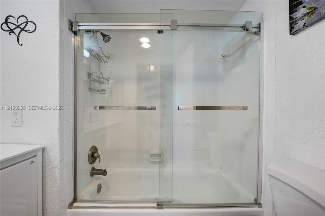 Bathtub and shower combination featuring a glass sliding door enclosure, white wall tile surround, and metallic finish faucet hardware