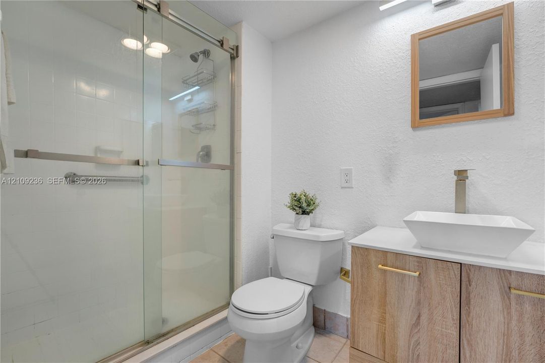 Bathroom featuring a wood-finish vanity with a rectangular vessel sink, sliding glass shower enclosure, and square-edged mirror