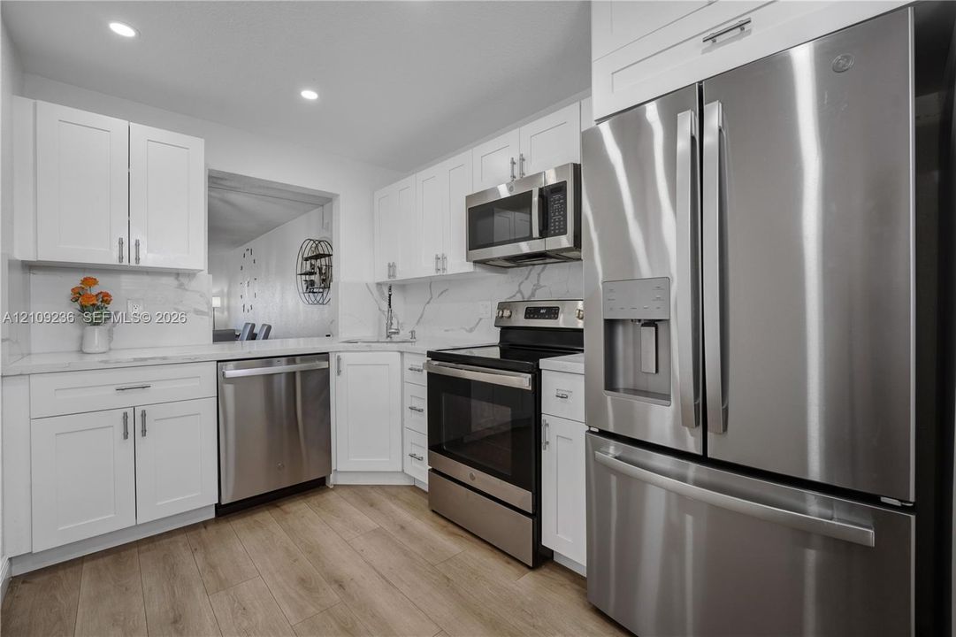 Kitchen featuring white shaker cabinetry, stainless steel appliances, stone-look countertops with integrated backsplash, and wood-finish flooring