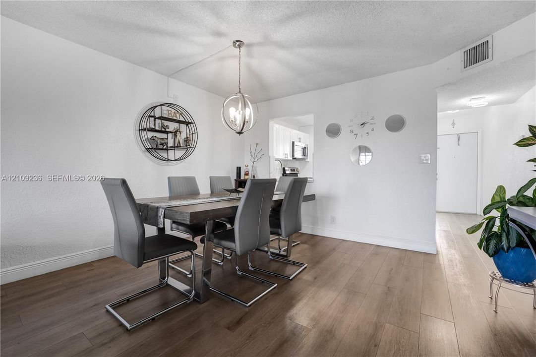 Dining area featuring wood-finish flooring, a multi-light spherical pendant fixture, and a pass-through opening to the kitchen