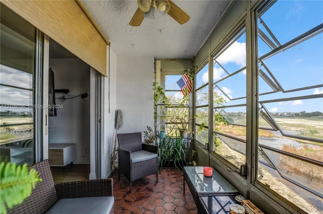 Enclosed sunroom featuring floor-to-ceiling multi-pane windows, hexagon-tile flooring, and a ceiling-mounted fan