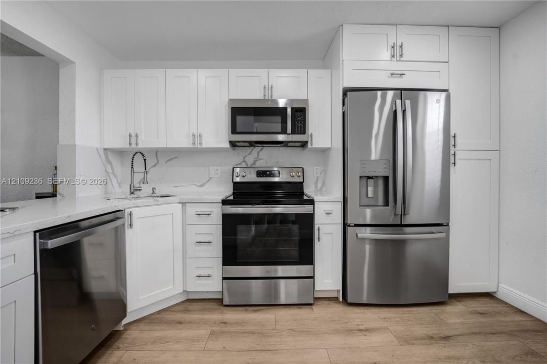 Kitchen featuring white shaker-style cabinetry, stainless steel appliances, stone-surface countertops, a stone-patterned backsplash, and wood-finish flooring