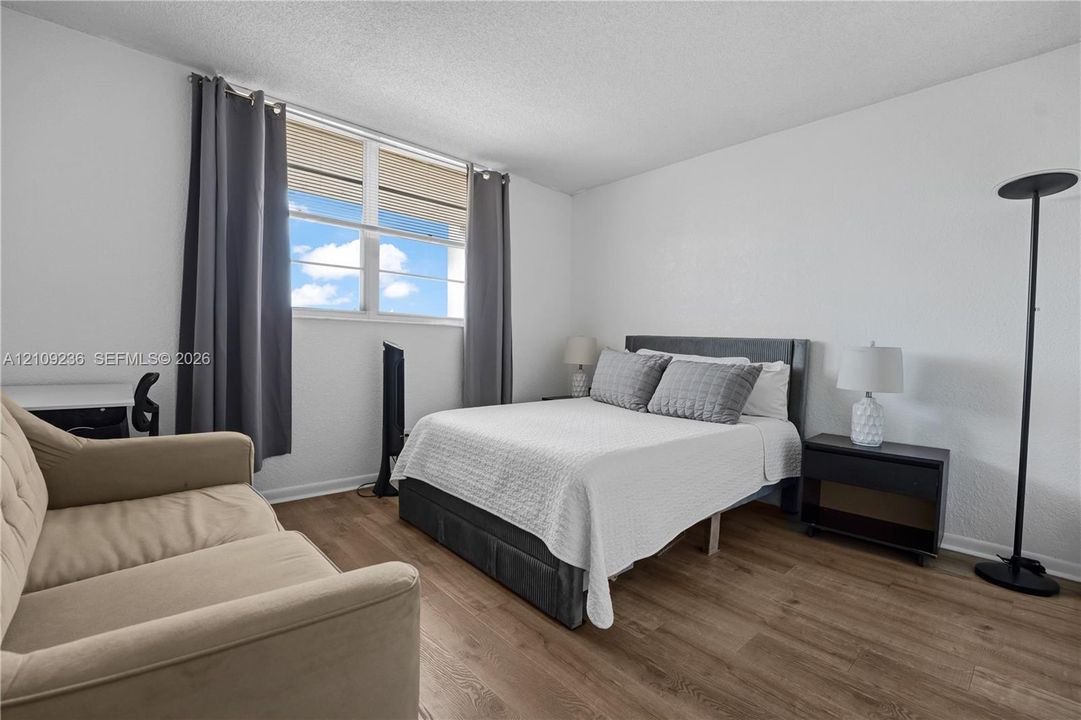 Bedroom featuring wood-finish flooring, textured walls, and a large horizontal window
