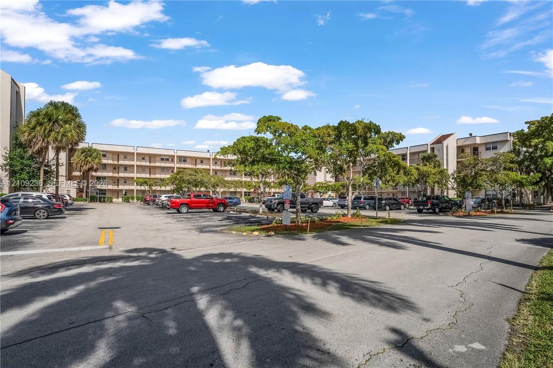 Multi-story residential building with paved surface parking, covered walkways, and mature palm and hardwood trees