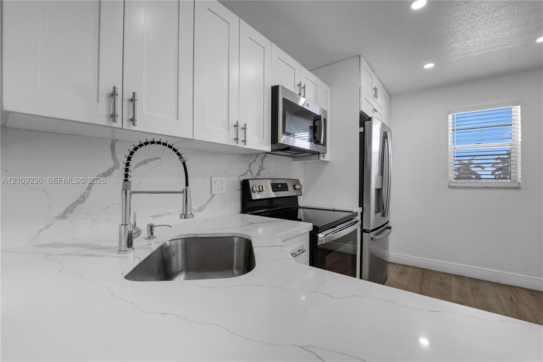 Kitchen featuring white shaker-style cabinetry, quartz countertops with veining, full-height stone backsplash, stainless steel appliances, and a high-arch pull-down faucet