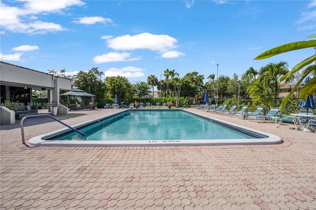 Rectangular swimming pool featuring a concrete paver deck, metal handrail, and poolside gazebo