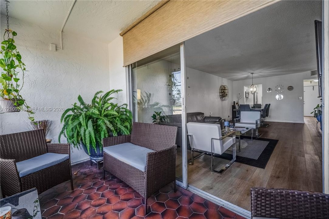 Covered balcony featuring hexagonal tile flooring and a retractable shade, opening via sliding glass doors to an interior with wood-finish flooring