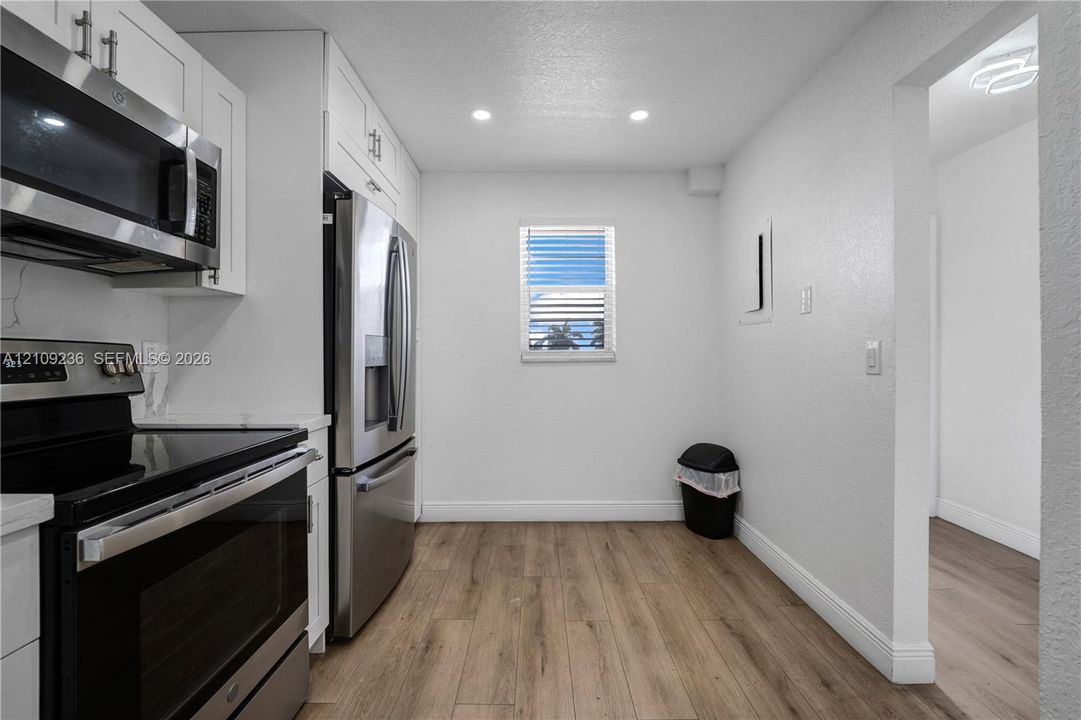 Kitchen featuring white shaker-style cabinetry, stainless steel appliances, wood-finish flooring, and recessed ceiling lighting