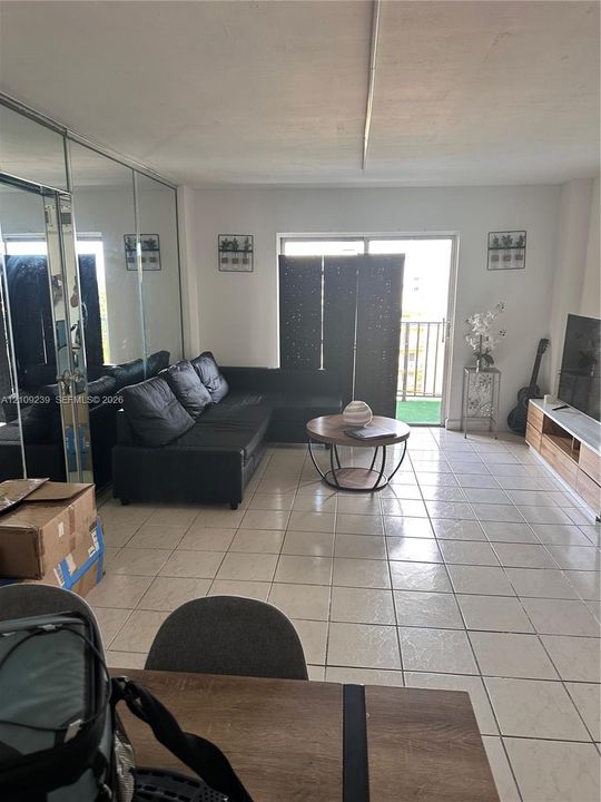 Living area featuring large-format ceramic tile flooring, floor-to-ceiling mirrored wall paneling, and a sliding glass door providing external access