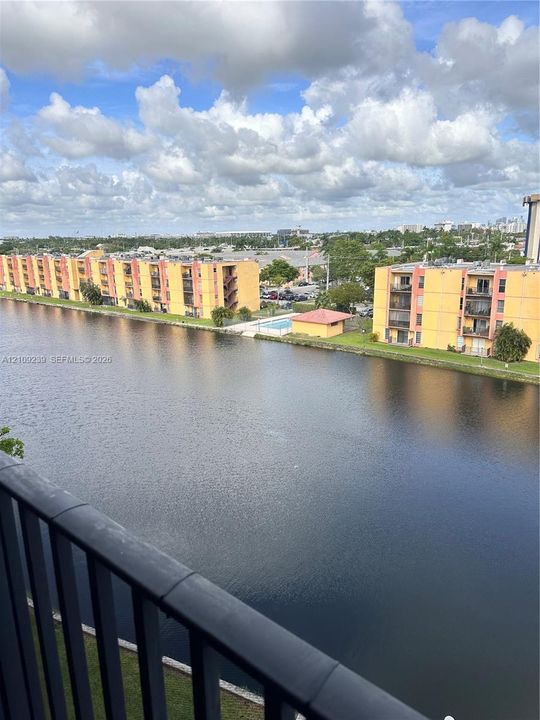 Exterior balcony featuring a black metal railing overlooking a waterfront setting with expansive canal waters and surrounding residential structures