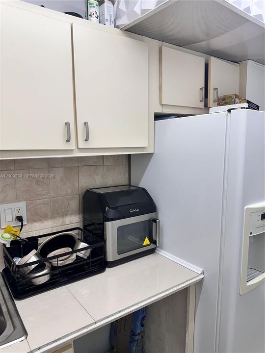 Kitchen area featuring light-toned cabinetry, a square-tile backsplash, and a white refrigerator with a built-in water and ice dispenser