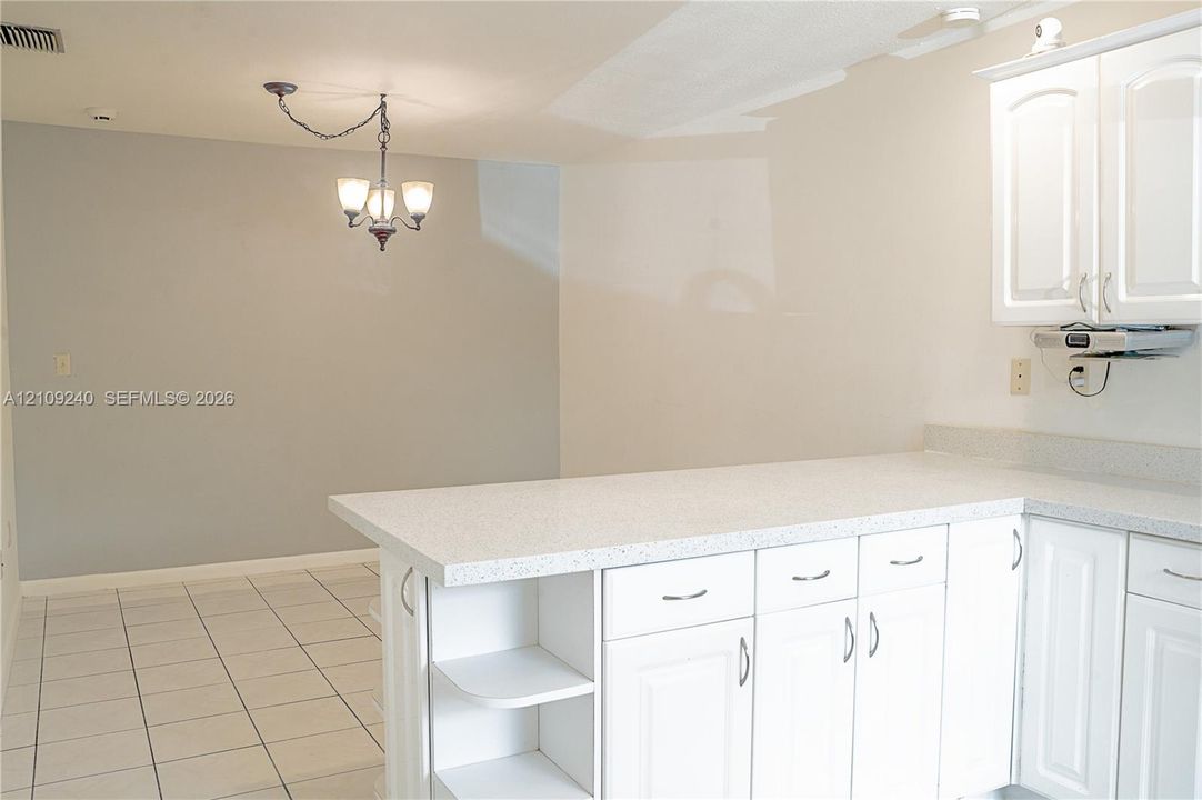 White cabinetry with integrated shelving, stone-finish countertops, tile flooring, and a multi-light chandelier