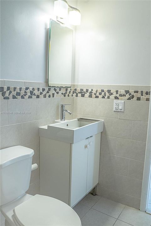 Wall-mounted vanity featuring a rectangular integrated sink, polished chrome faucet, tiled backsplash with mosaic accent border, and dual-light vanity fixture